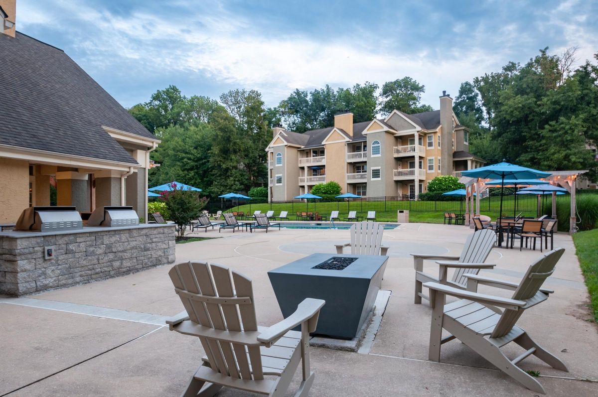 Outdoor pool area with lounge chairs, fire pit, grills, and apartment buildings in the background.