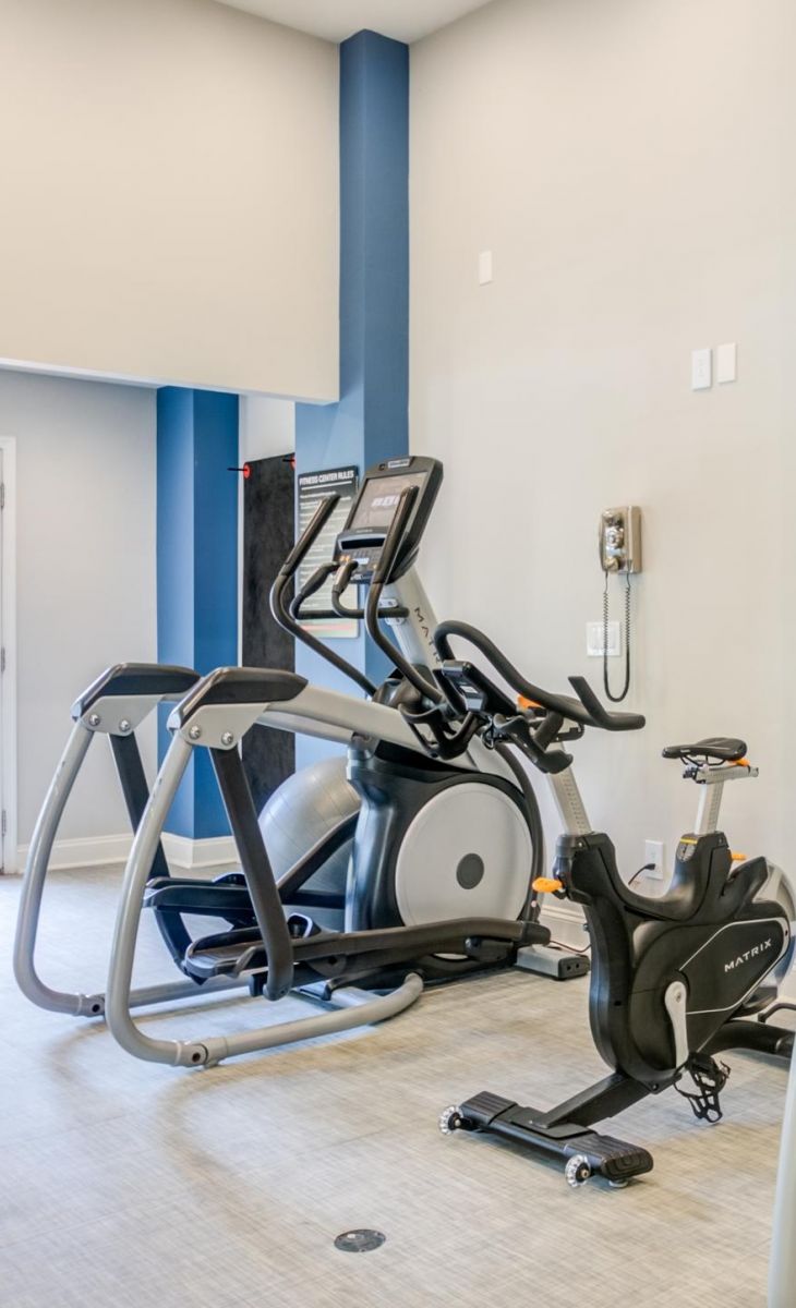 Elliptical machine and stationary bike in a bright, modern gym with light walls and blue accents.