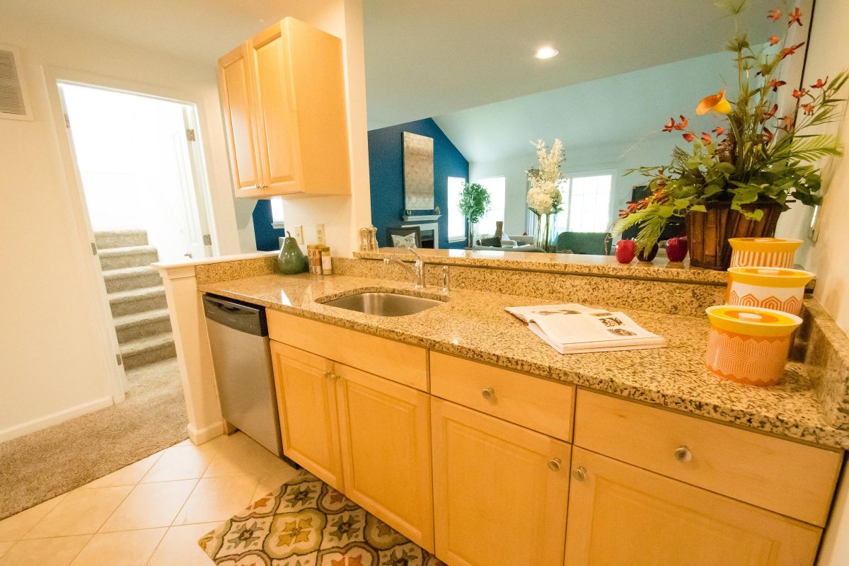 Modern kitchen with granite countertops, light wood cabinets, sink, and view into a carpeted living area.
